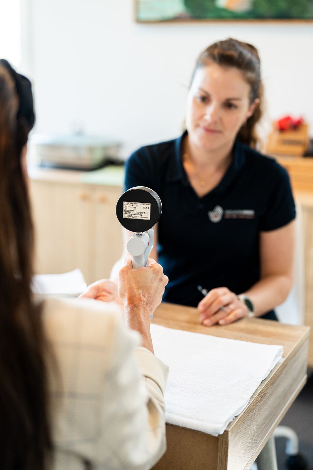 A patient using a pinch gauge while Danielle Crestani records the result